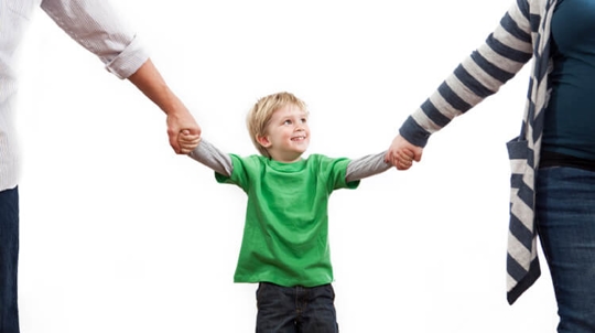 A small blond child in a green shirt holds each of his parents' hands. The parents are out of frame on each side of the image.