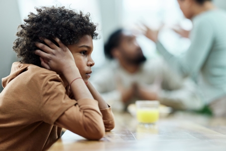 child covering his ears in front of fighting parents