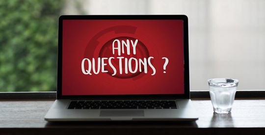 An open laptop sits in front of a window next to a glass of water. The screen is red with white text spelling "Any questions?"