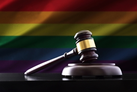 Judge mace on wooden base on black table with LGBT flag background. Front view.