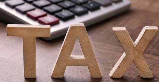 Wooden letters that spell "tax" with a calculator in the background.